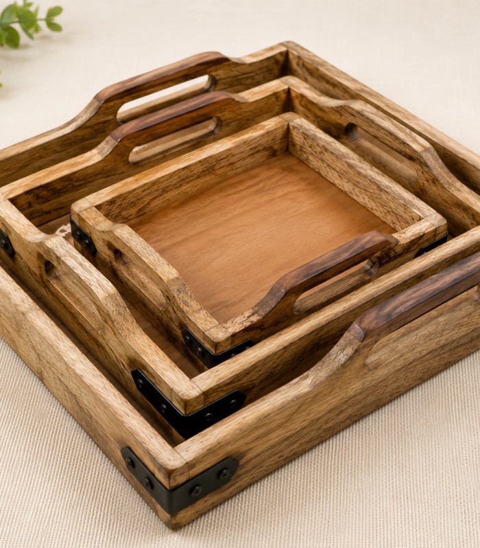 Set of three handcrafted mango wood nesting serving trays in large (12 inches), medium (10 inches), and small (8 inches) sizes with cutout handles and rustic iron corner accents.